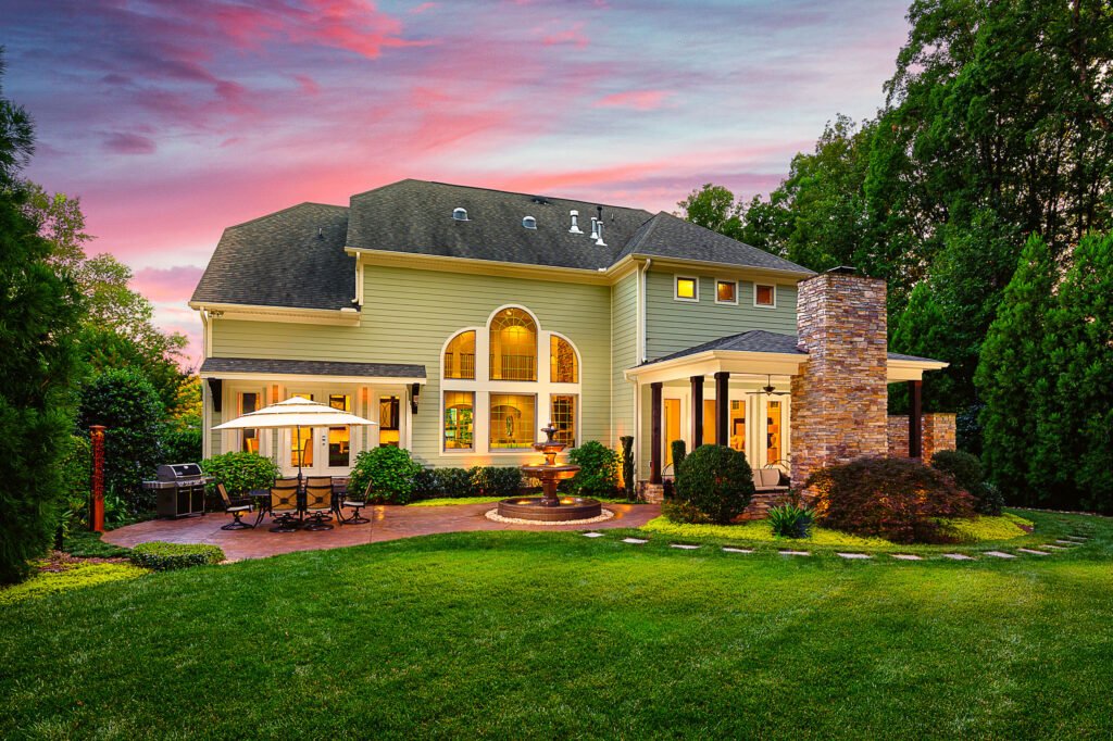 Rear exterior with a stone fireplace and fountain at twilight