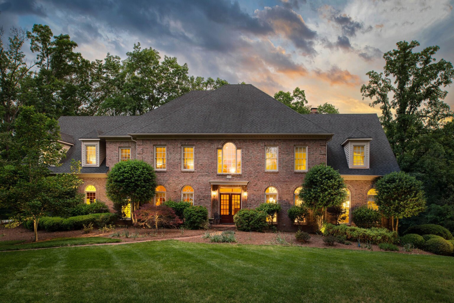 Brick colonial estate photographed at twilight with a dramatic sky